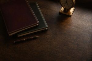 Dos expedientes de cuero de colores distintos sobre mesa de roble con pluma y reloj, evocando la prejudicialidad penal entre proceso civil y penal