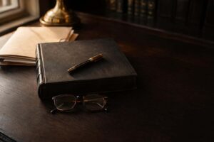 Libro de derecho cerrado en cuero negro con pluma estilográfica antigua y gafas dobladas sobre mesa de roble oscuro, evocando la responsabilidad penal