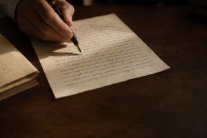 Mano sosteniendo una pluma sobre un documento manuscrito en una mesa de despacho oscura, escena editorial sobria que evoca un delito doloso